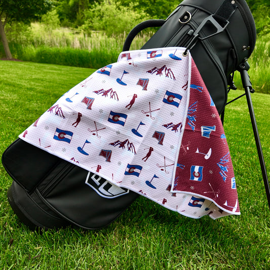 Colorado Avalanche golf towel hanging on a black golf bag with white back pattern, Colorado flags, mountains, skis, golfers, snowflakes, and golf flag icons.