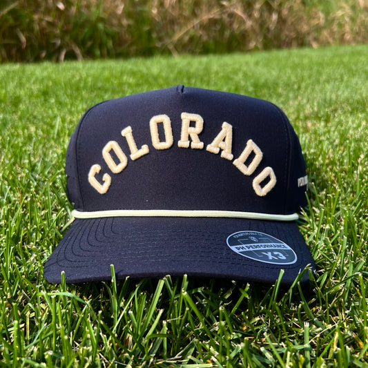 Black Colorado performance golf hat on grass with cream raised Colorado script embroidery, cream rope, flat brim, and PH Performance X3 sticker.