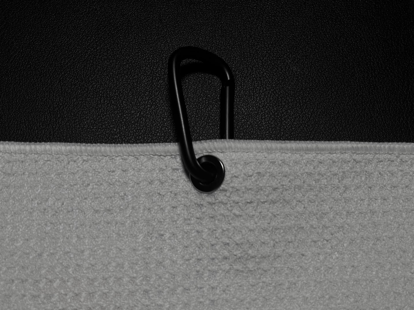 Close up product detail of a golf towel carabiner clip and towel edge against a black golf bag.