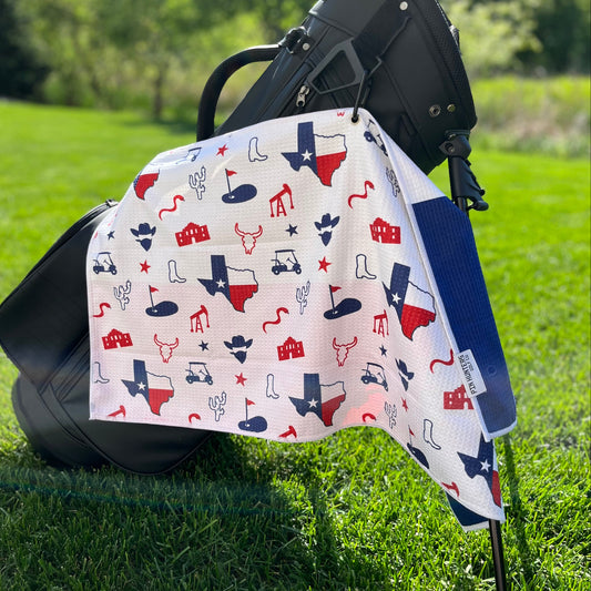 Lone Star Texas flag themed golf towel hanging from a black golf bag with red and blue Texas state, boot, longhorn, oil, cactus, Alamo, and golf icons.