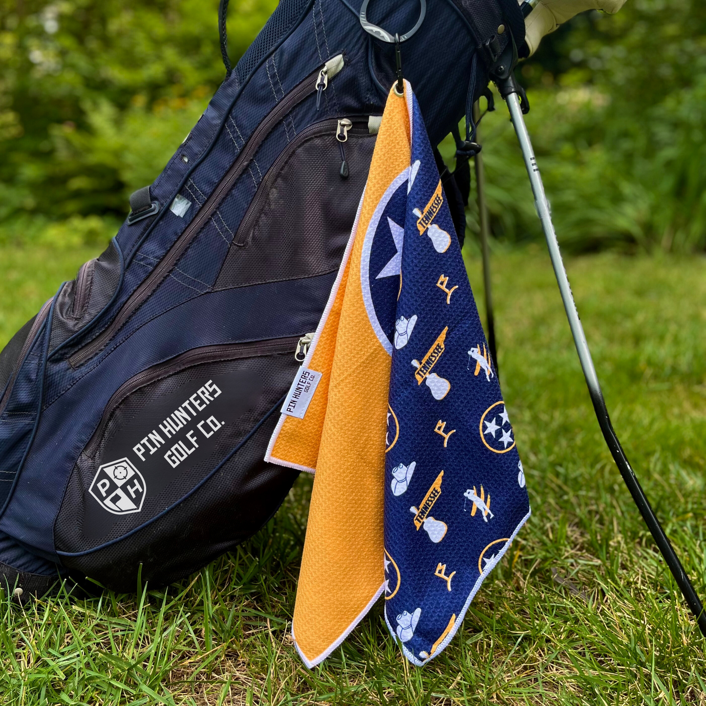 Navy and gold Tennessee golf towel hanging from golf bag with tristar icons, golf graphics, white trim, and gold waffle-texture back.