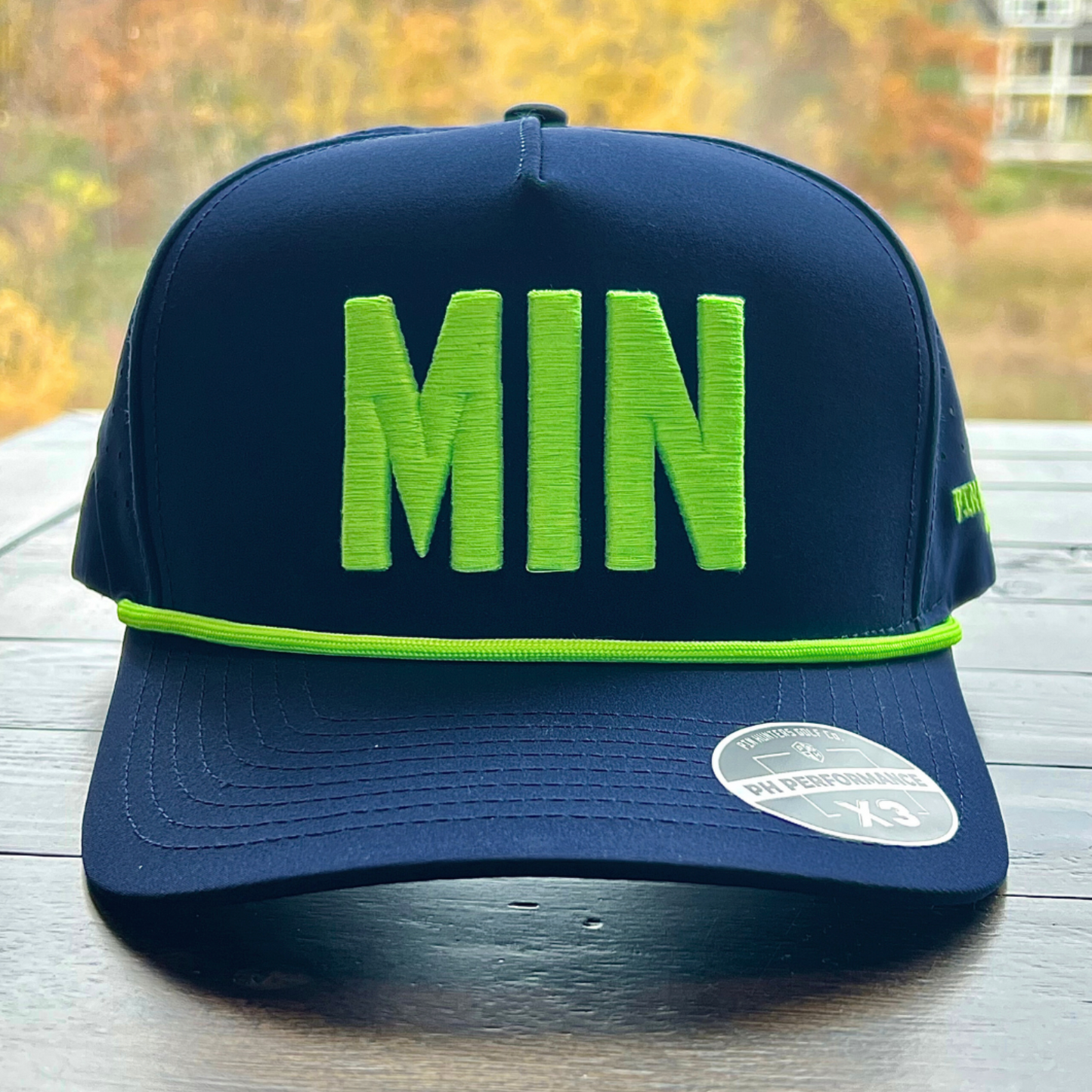 Front view of navy MIN performance golf hat with neon lime raised MIN embroidery, matching rope, flat brim, and PH Performance X3 sticker.