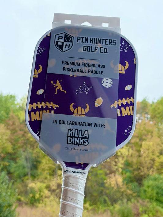 Purple Minnesota pickleball paddle in retail packaging with gold Viking helmet graphics, football icons, MIN text, playbook details, and Killa Dinks collaboration label.