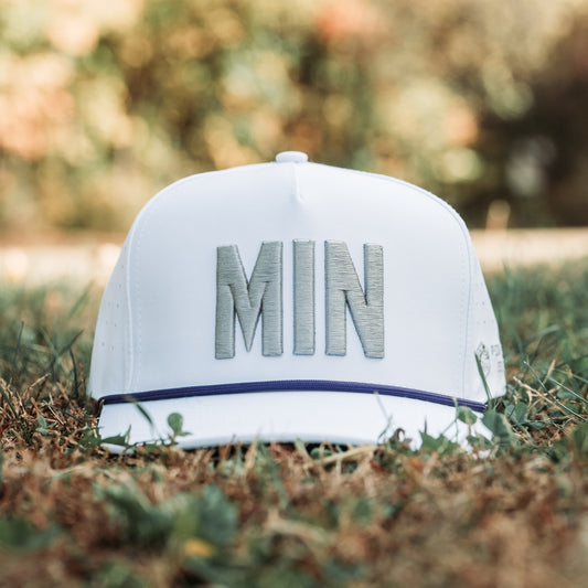 White MIN vikings whiteout warrior performance golf hat on grass with gray raised MIN embroidery, purple rope detail, perforated side panels, and clean tonal design.