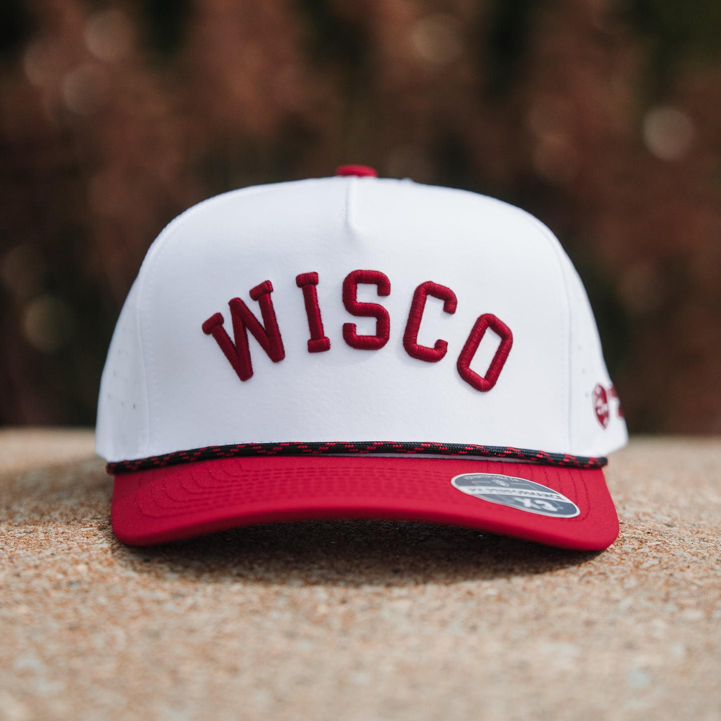 White Wisco performance golf hat front view with red raised embroidery, red brim, black and red rope detail, and PH Performance X3 sticker.