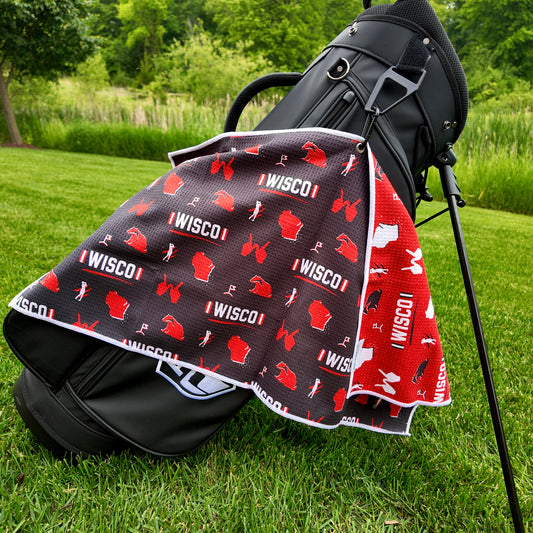Wisconsin Badgers black golf towel hanging on a black golf bag with I WISCO text, red Wisconsin outlines, badger graphics, golfers, golf flags, and red reverse side.