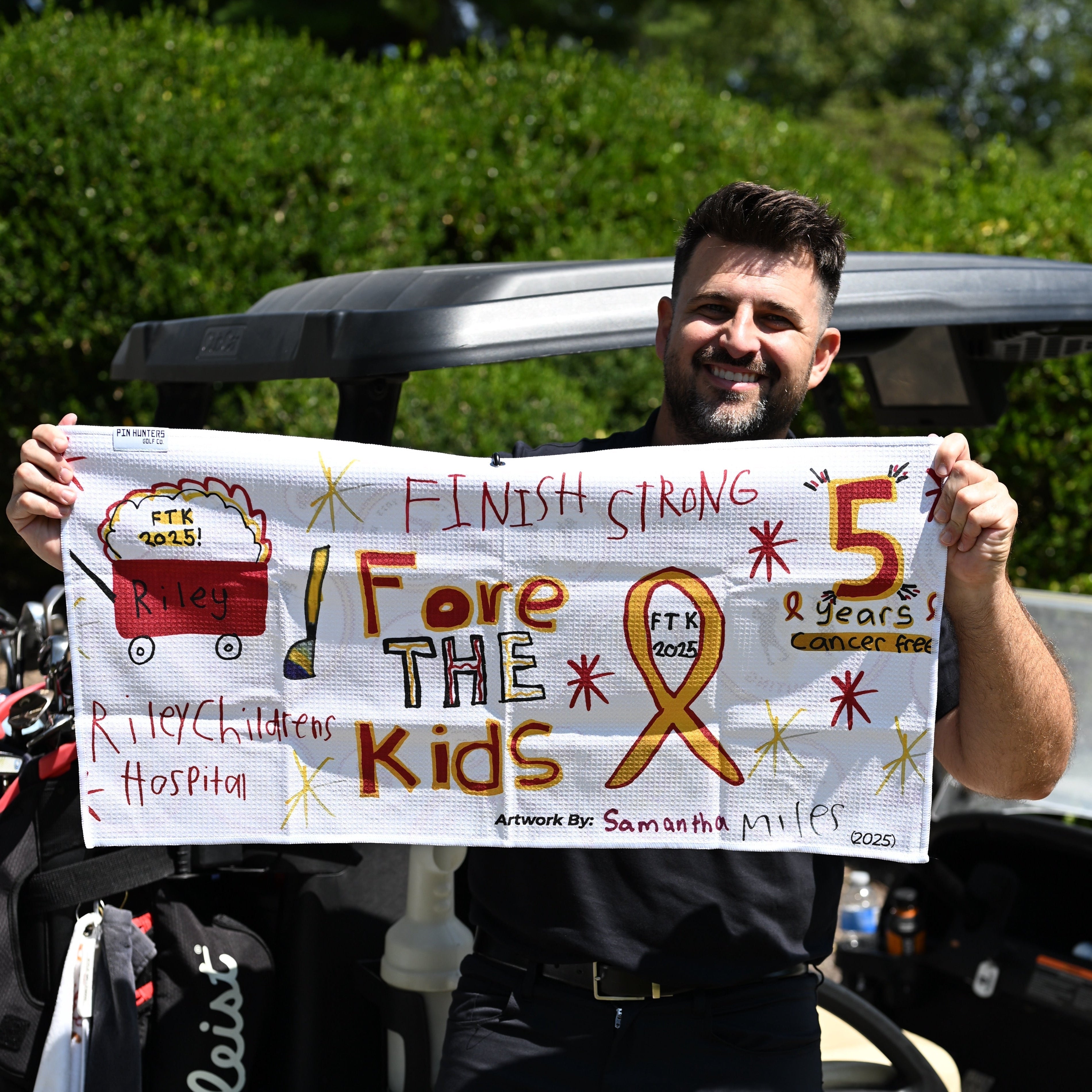 Man holding a custom Pin Hunters Golf Towel standing in front of a golf cart.
