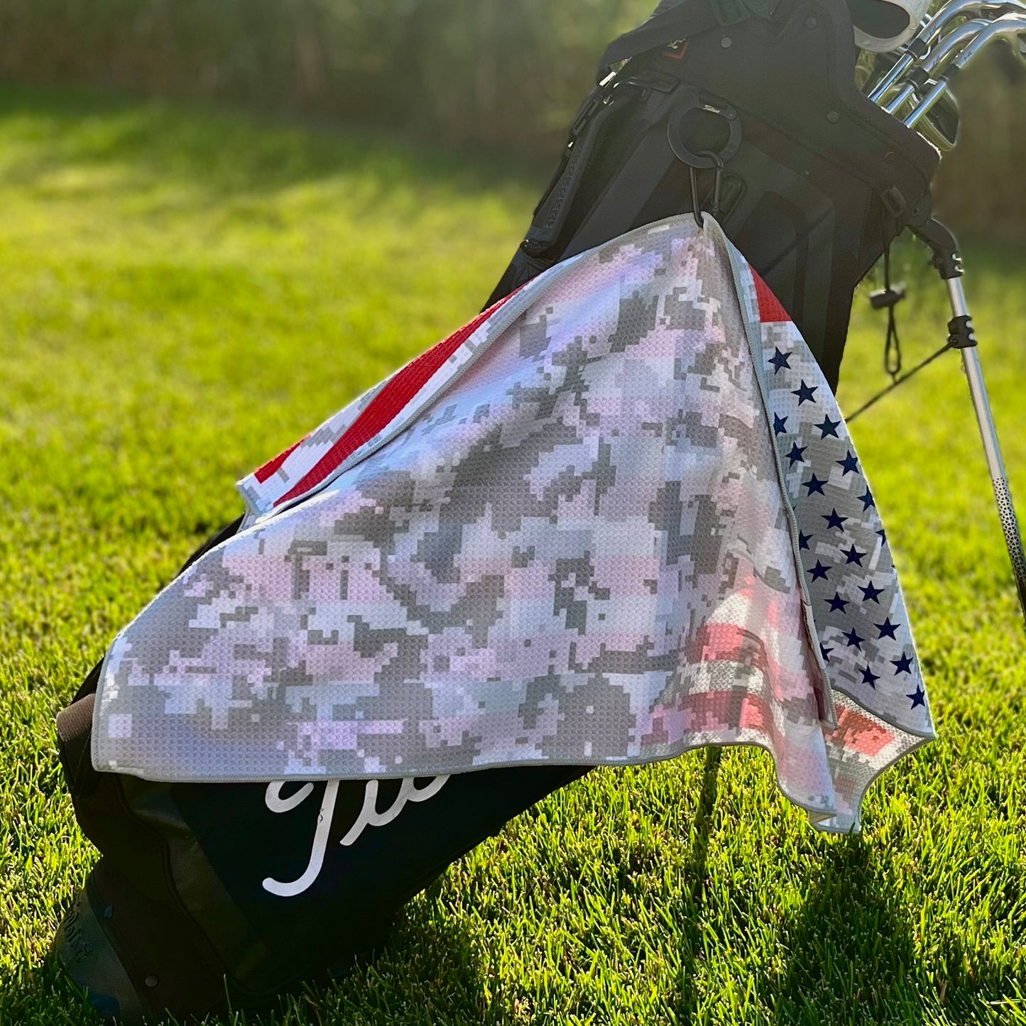 American flag golf towel hanging from a golf bag showing the gray digital camo reverse side with blue stars and red stripe details.