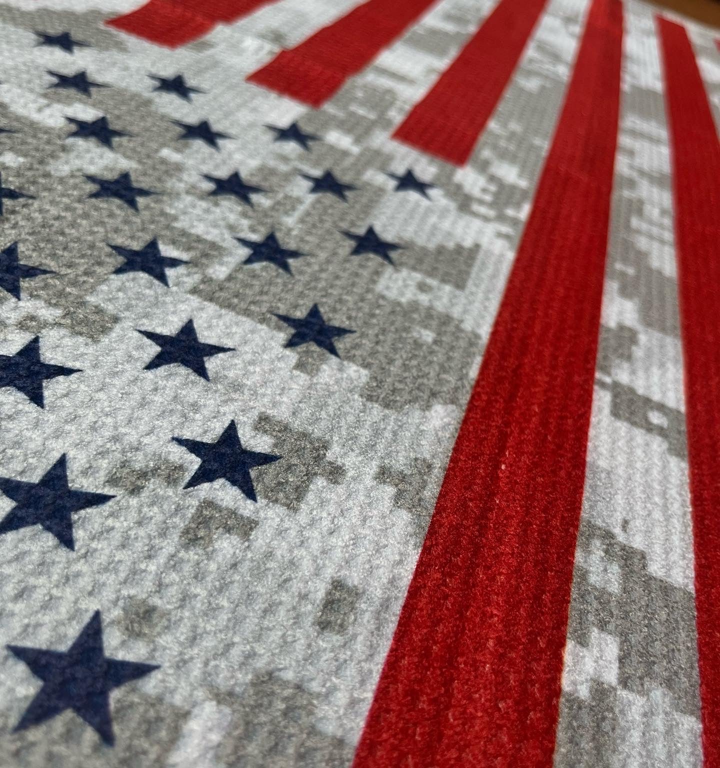 Close up of an American flag golf towel showing blue stars, red stripes, gray digital camo print, and microfiber waffle fabric texture.