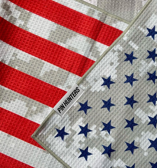 Close up of an American flag golf towel showing the Pin Hunters label, red stripes, blue stars, gray digital camo, and waffle microfiber texture.
