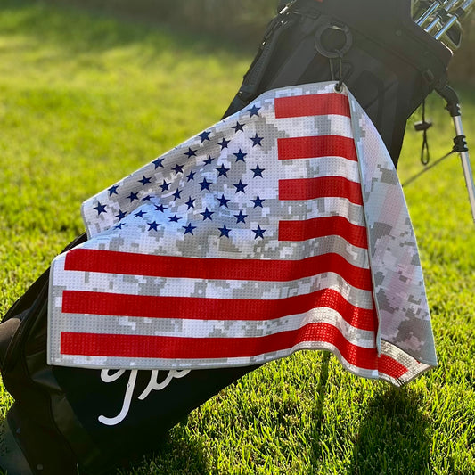 American flag golf towel with red stripes, blue stars, and gray digital camo pattern hanging from a golf bag.