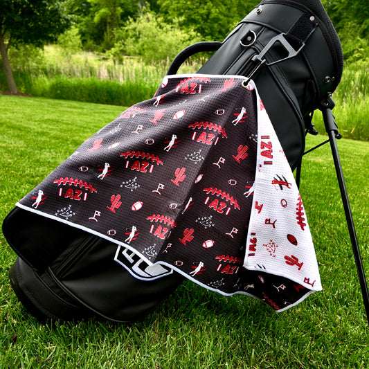 Arizona Cardinals black golf towel hanging on a black golf bag with red AZ football graphics, cactus icons, golfers, footballs, playbook, and white reverse side.