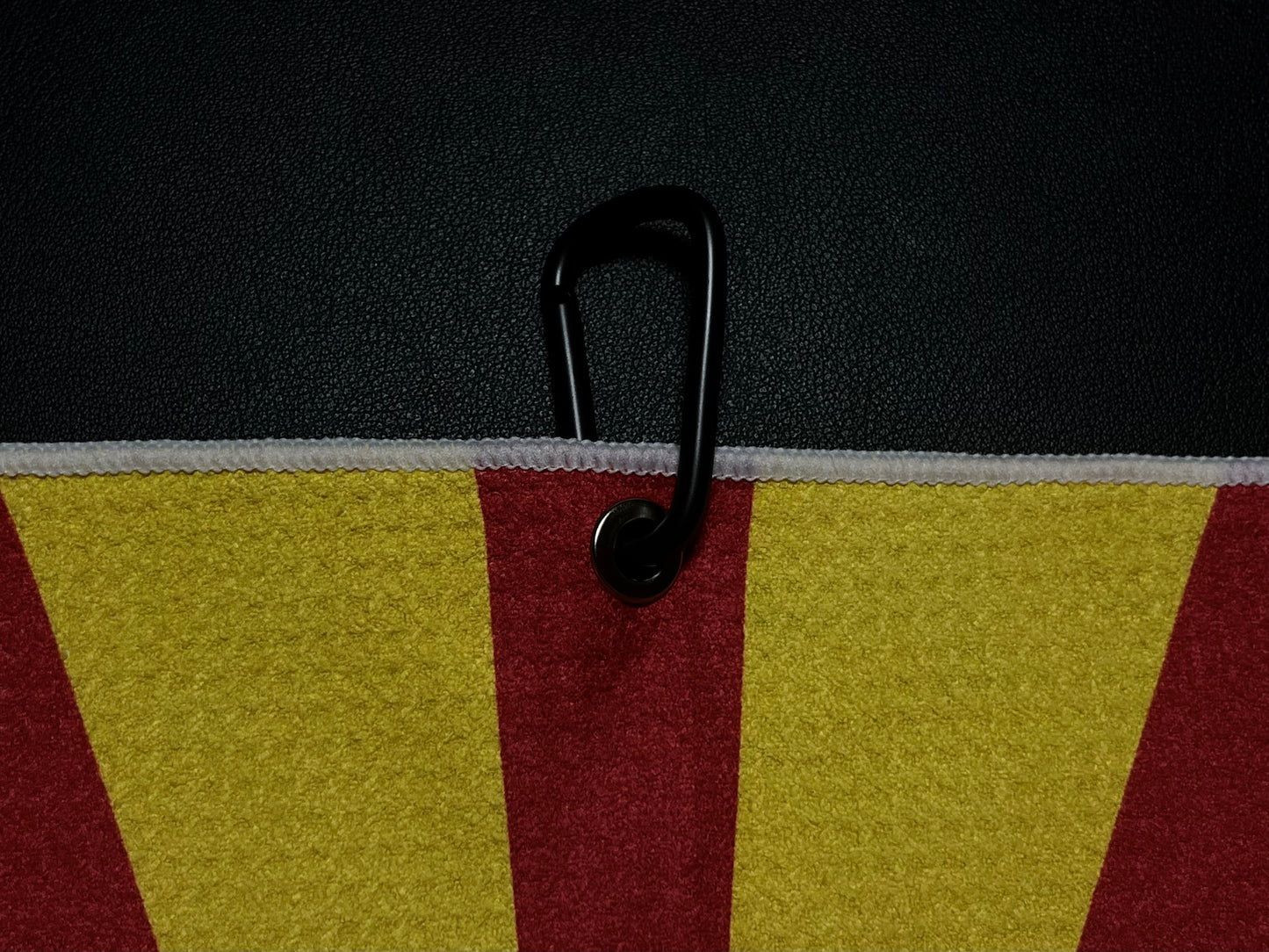Close up of a black carabiner clipped to an Arizona flag inspired golf towel showing red, gold, and white microfiber fabric.