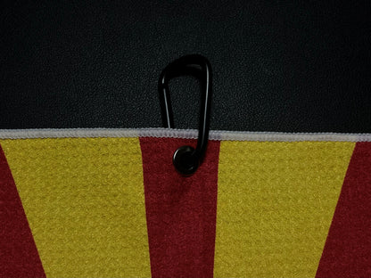 Close up of a black carabiner clipped to an Arizona flag inspired golf towel showing red, gold, and white microfiber fabric.