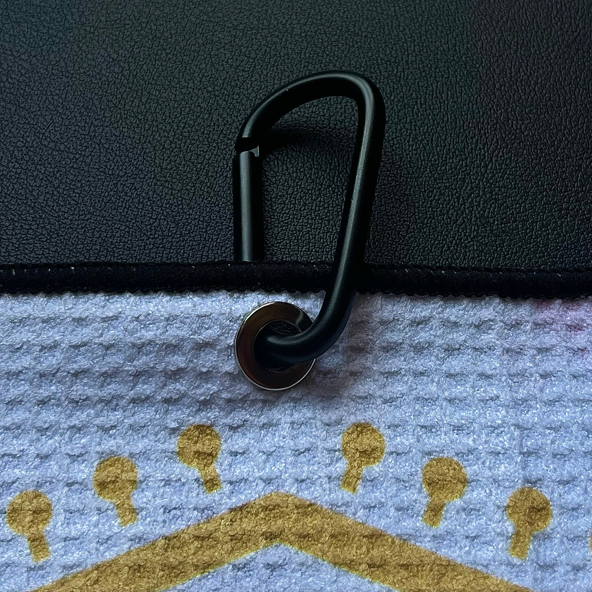 Close up of a black carabiner clipped to an Arizona flag inspired golf towel with red, gold, and blue printed details.