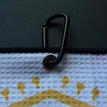 Close up of a black carabiner clipped to an Arizona flag inspired golf towel with red, gold, and blue printed details.