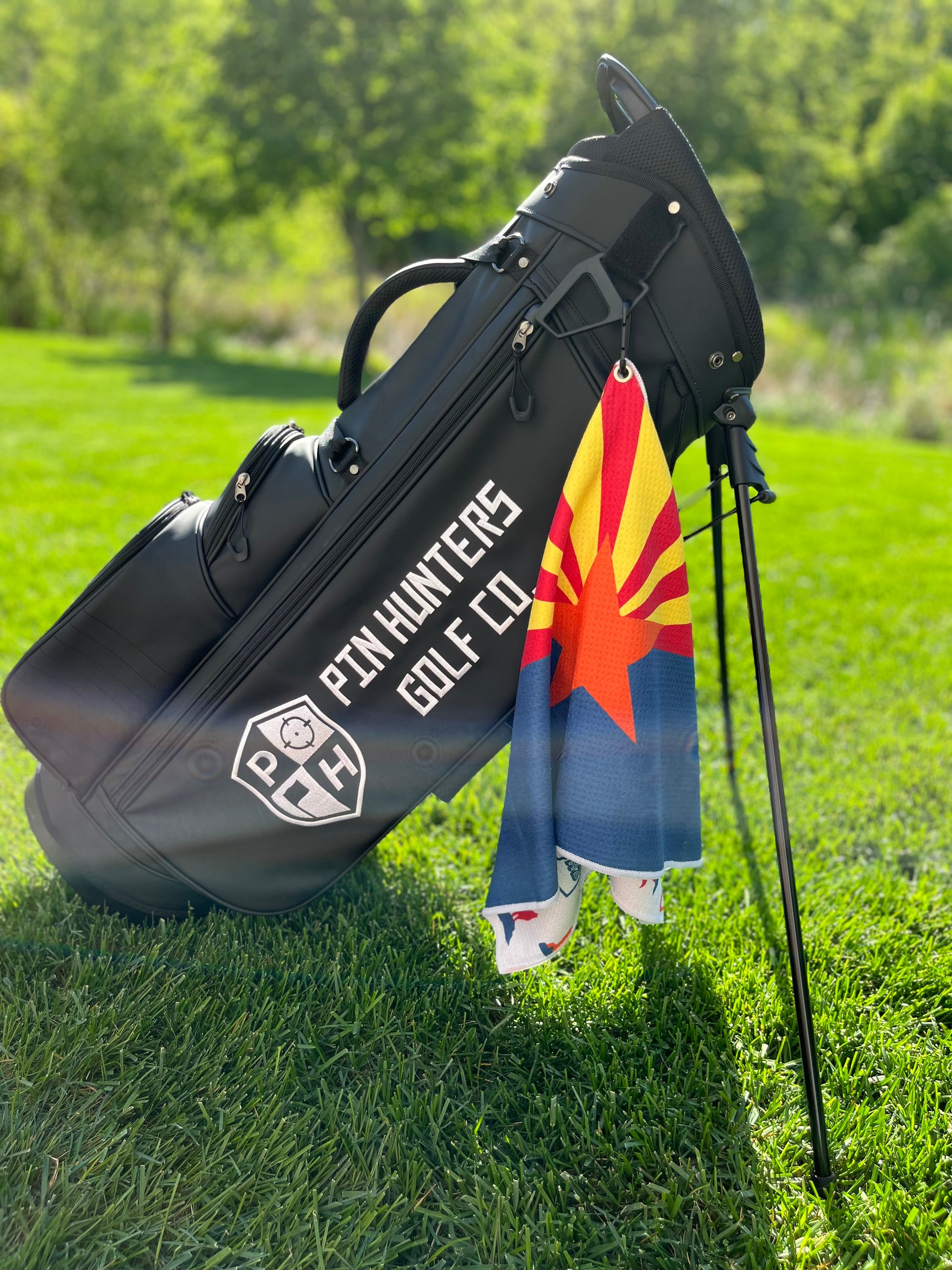 Arizona flag inspired golf towel hanging from a black Pin Hunters golf bag with red, gold, orange, and blue state flag colors.