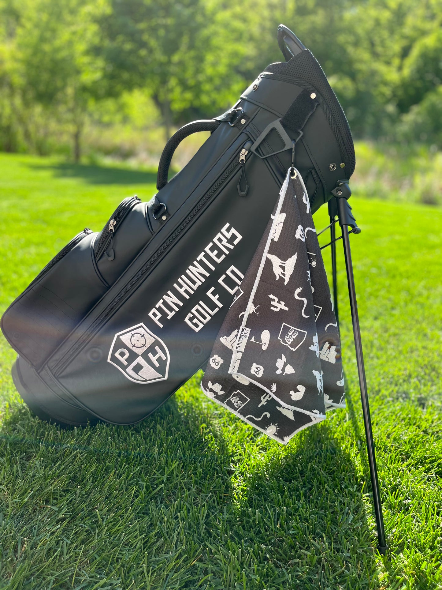 Black Arizona themed golf towel hanging from a black Pin Hunters golf bag with white desert, cactus, AZ state, Route 66, sun, and golf icons.