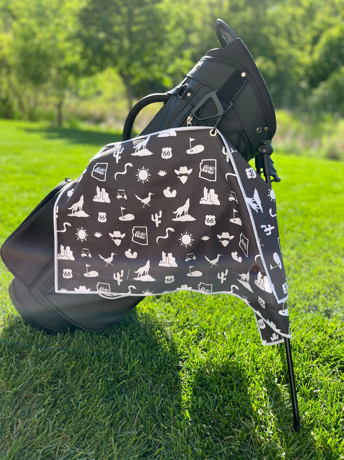 Black Arizona themed golf towel hanging from a black Pin Hunters golf bag with white desert, cactus, Route 66, AZ state, sun, golf cart, and golf icons.