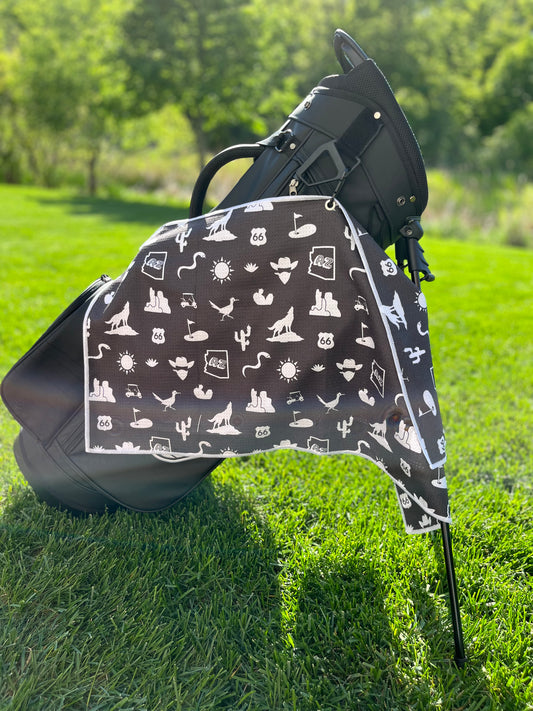 Black Arizona themed golf towel hanging from a black Pin Hunters golf bag with white desert, cactus, Route 66, AZ state, sun, golf cart, and golf icons.