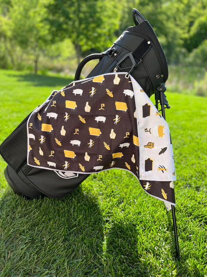Black and gold Iowa Hawkeyes inspired golf towel hanging from a black golf bag with Iowa state, corn, pig, foam finger, and golf flag graphics.