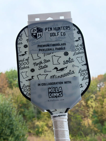 Black and white Minnesota pickleball paddle in retail packaging with loon graphics, Minnesota outlines, North Star State text, and Killa Dinks collaboration label.
