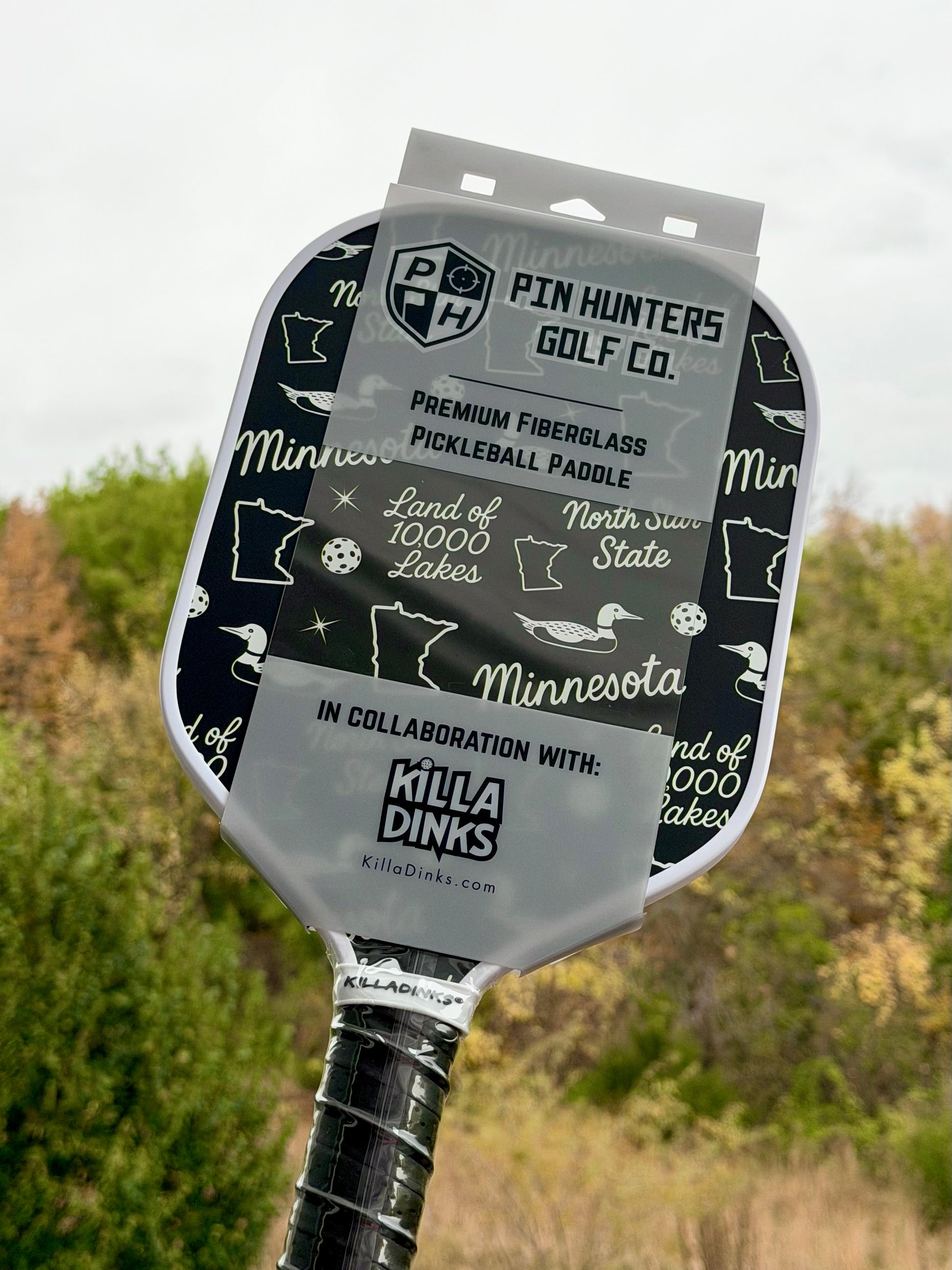 Black Minnesota pickleball paddle with white Land of 10,000 Lakes, loon, Minnesota, and North Star State graphics in Killa Dinks packaging.