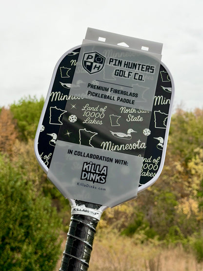 Black Minnesota pickleball paddle with white Land of 10,000 Lakes, loon, Minnesota, and North Star State graphics in Killa Dinks packaging.