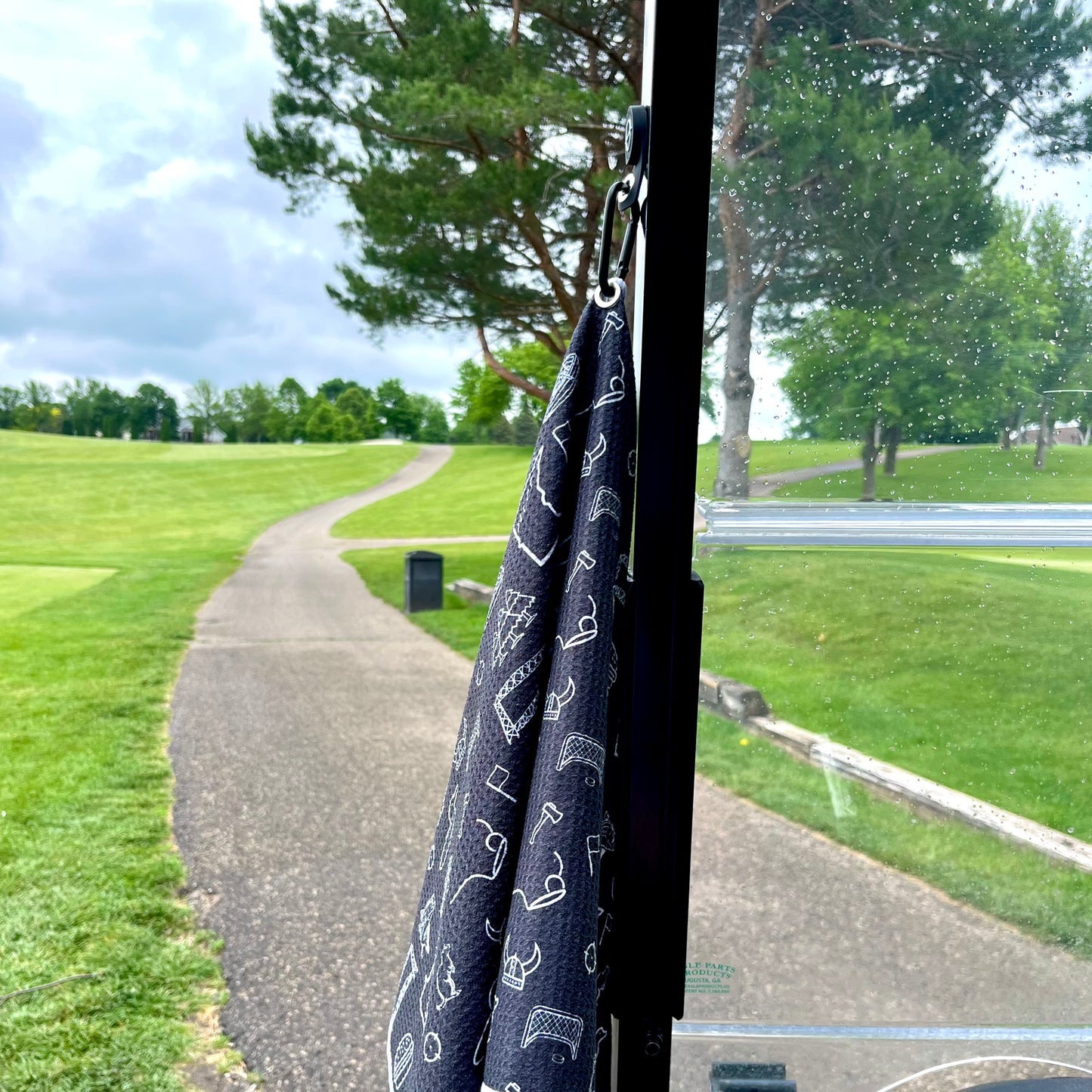 Black patterned golf towel hanging from a golf cart with white state, boot, flag, and golf themed icons visible through the cart windshield.