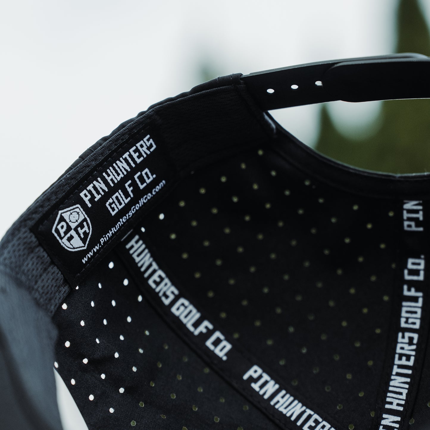 Inside view of black Pin Hunters Golf Co. performance hat with branded inner label, black sweatband, perforated crown, and adjustable snapback closure.