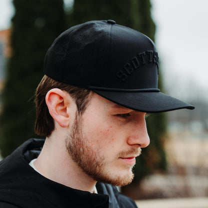 Black Scottsdale tonal performance golf hat on model with black raised embroidery, matching rope detail, and perforated side panels.