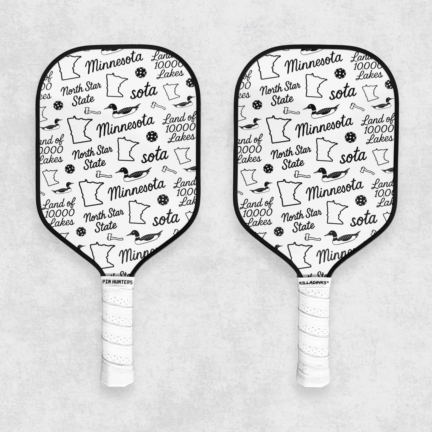 Black and white Minnesota pickleball paddle set with state icons, loons, pickleballs, and white grips on a gray textured background.