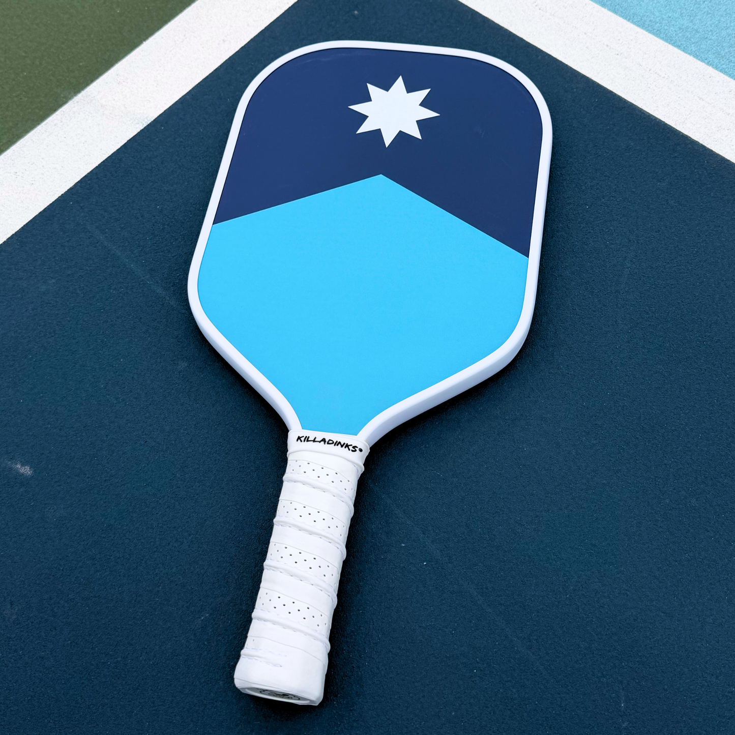 Blue Minnesota pickleball paddle on court with navy top section, light blue bottom section, white border, and north star design.