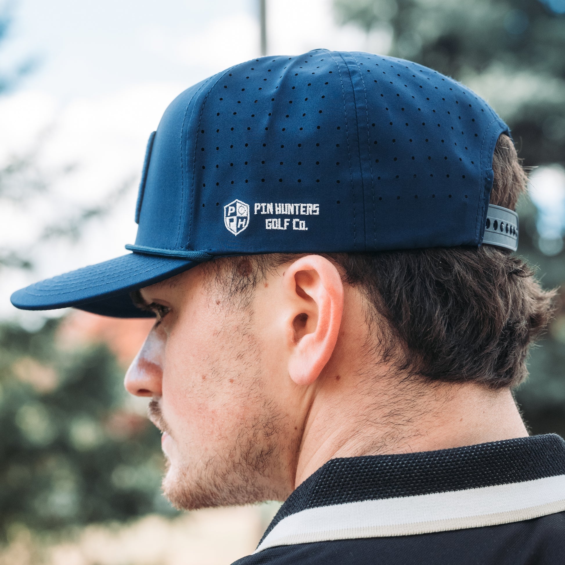 Blue tonal MIN performance golf hat with side logo embroidery, perforated panels, flat brim, and matching rope detail.