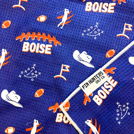Close up of Boise State golf towel with blue and orange Boise, football, cowboy hat, golfer, playbook, and golf flag graphics.