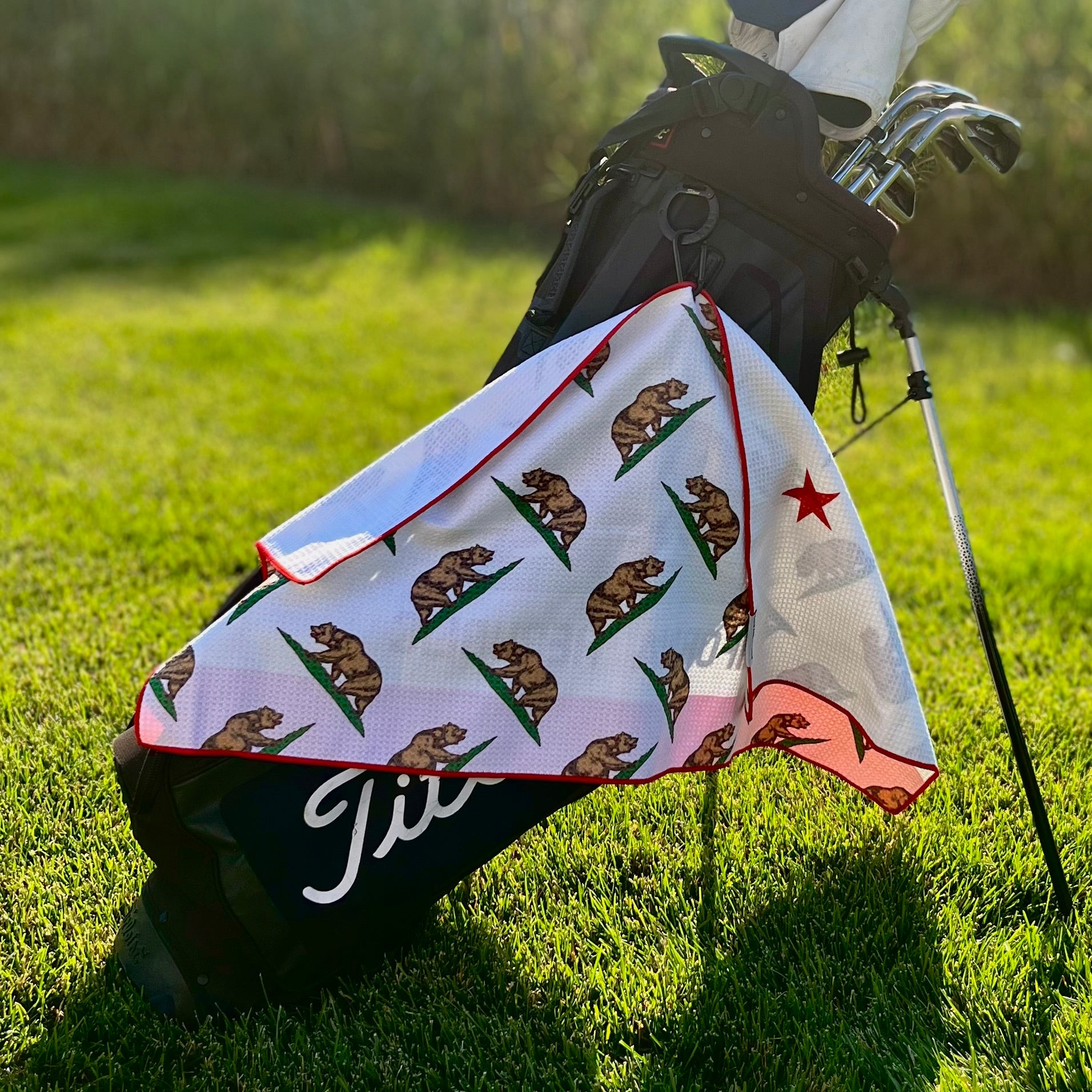 California Republic golf towel hanging from a golf bag showing the white side with repeating California bear graphics and red trim.