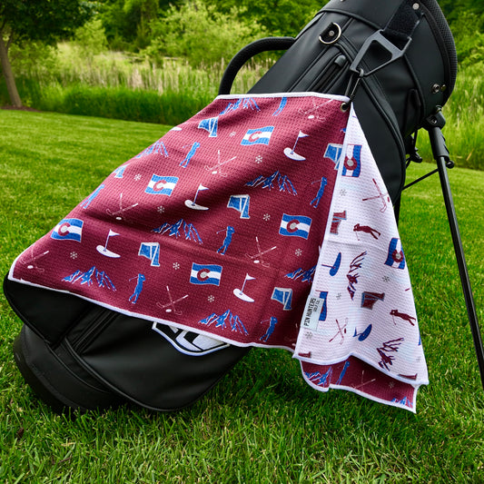 Colorado Avalanche golf towel hanging on a black golf bag with maroon back pattern, Colorado flag graphics, blue mountains, skiers, golf flags, clubs, and snowflakes.