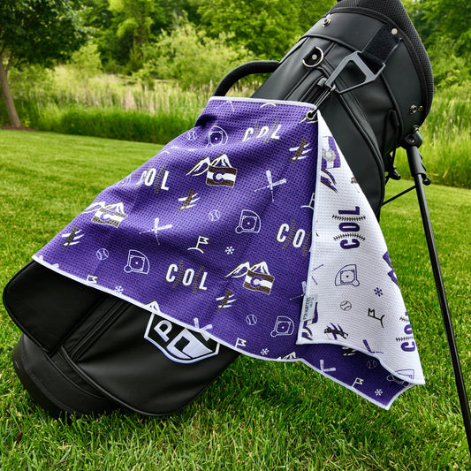 Colorado Rockies purple golf towel hanging on a black golf bag with COL text, mountain graphics, baseballs, skis, snowflakes, and golf icons.