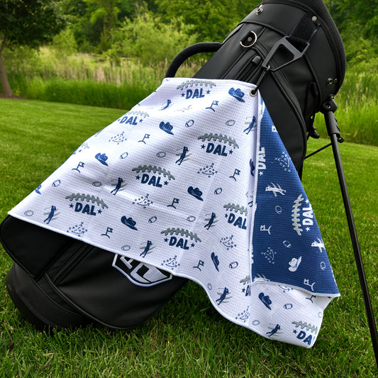 Dallas Cowboys white golf towel hanging on a black golf bag with DAL text, navy and gray football graphics, cowboy hats, golfers, playbook, and blue reverse side.