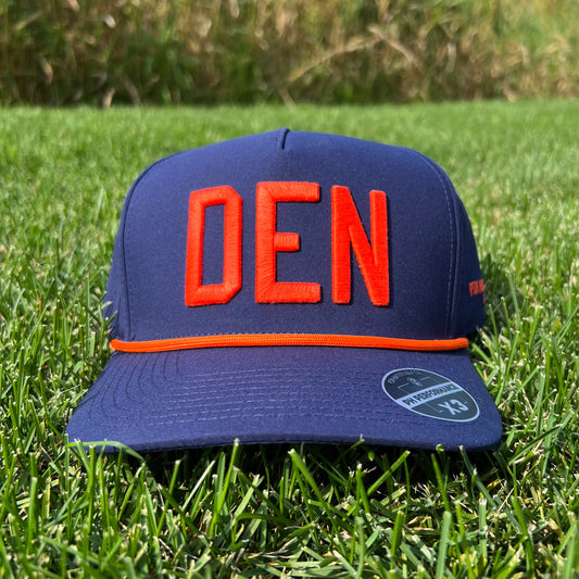 Navy Denver performance golf hat on grass with bright orange raised DEN embroidery, orange rope, flat brim, and PH Performance X3 sticker.