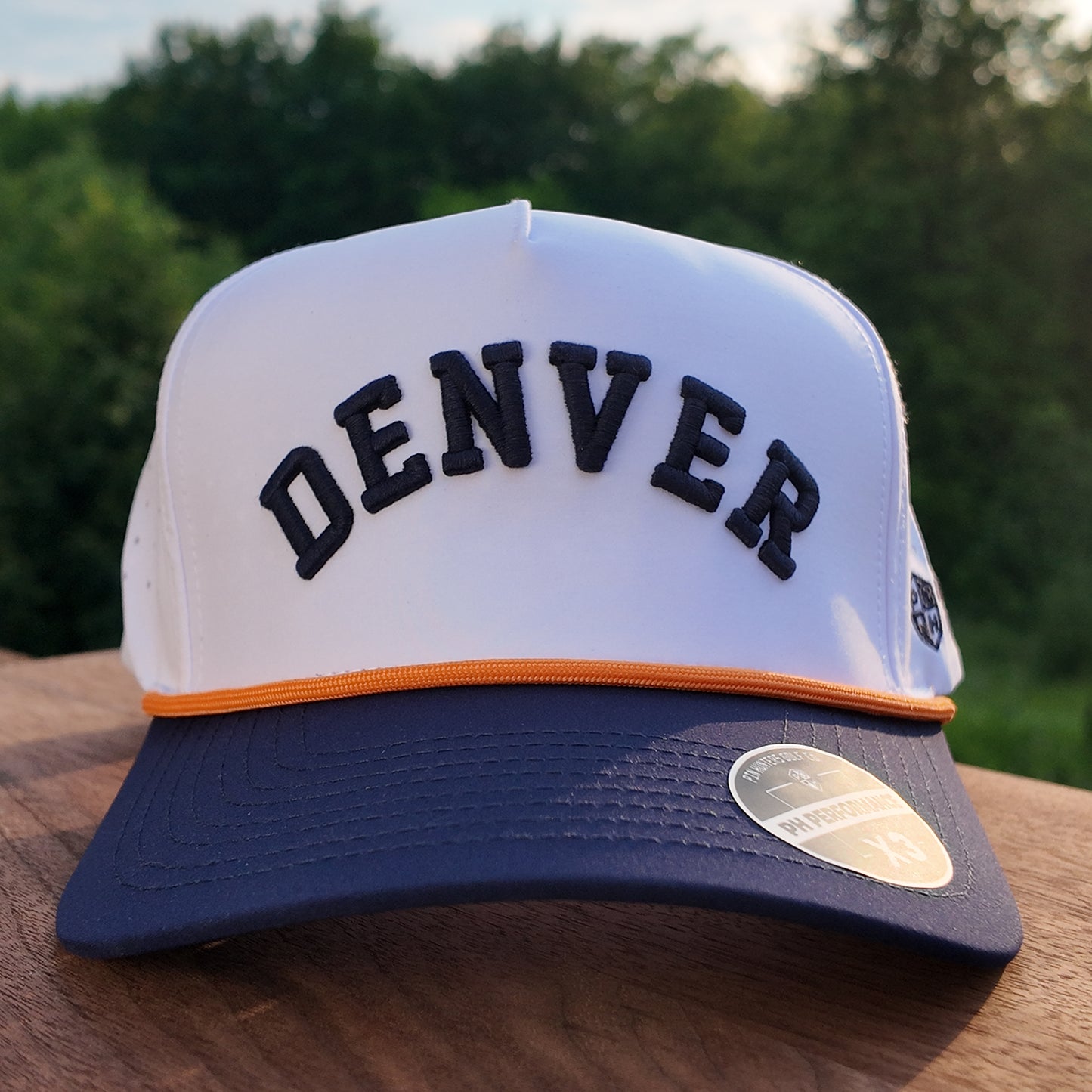 Front view of the Denver performance golf hat with black raised Denver embroidery, white crown, orange rope, navy brim, and PH Performance sticker.