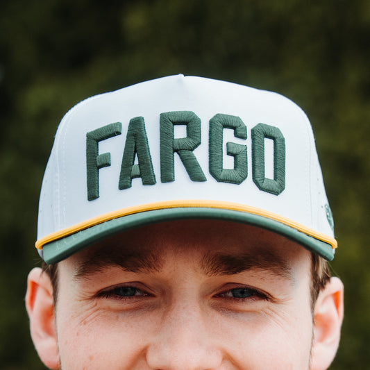 White Fargo performance golf hat with green raised FARGO embroidery, gold rope, green brim, and perforated side panels.