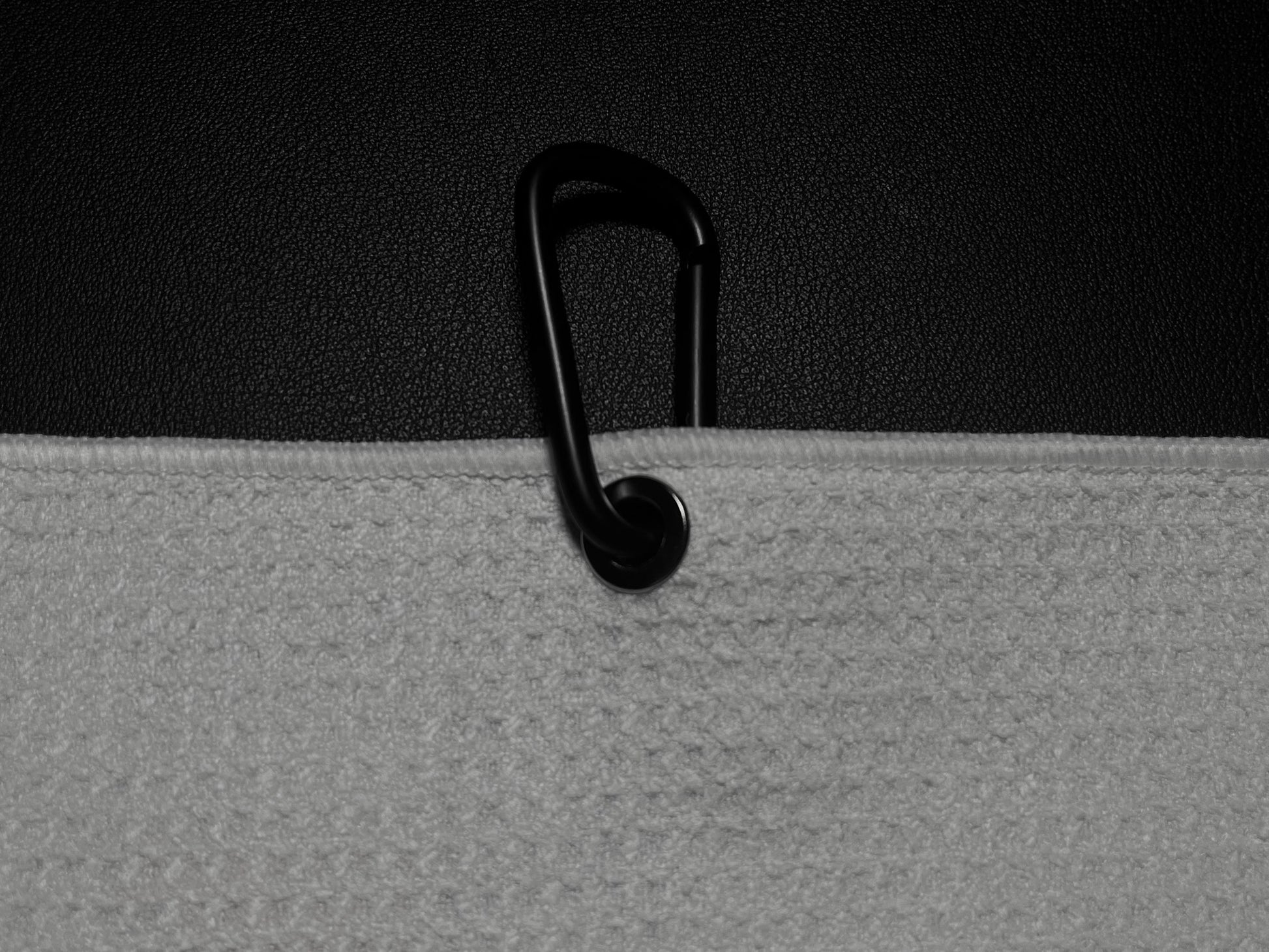 Close up product detail of a golf towel carabiner clip and towel edge against a black golf bag.