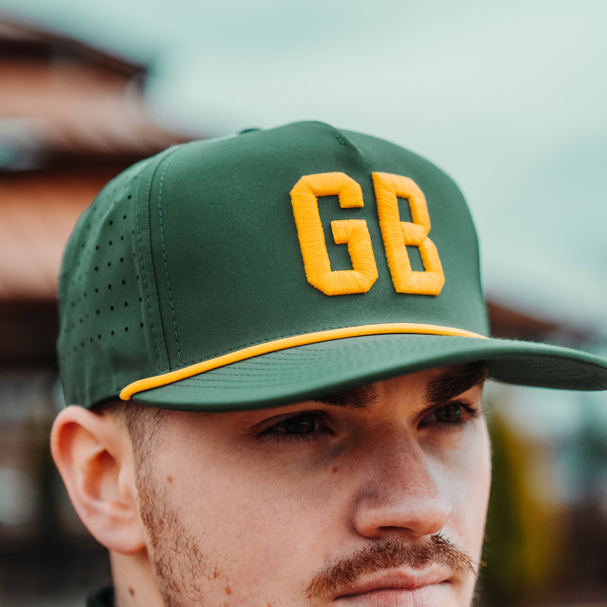Green Bay Packers GB performance hat lifestyle view with green crown, yellow raised embroidery, yellow rope, flat brim, and perforated side panels.