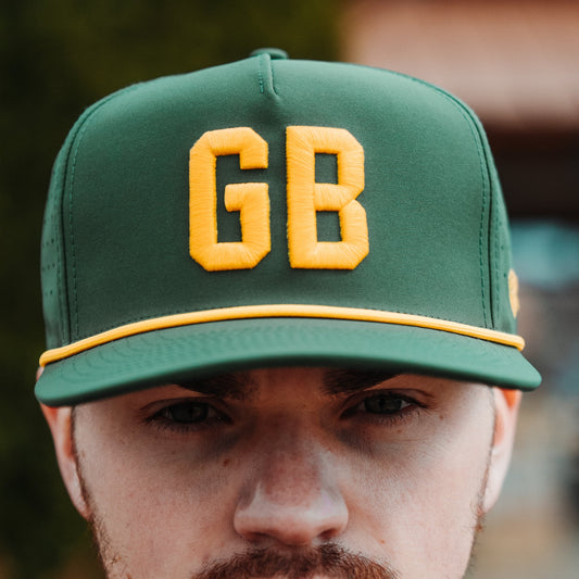 Green GB performance golf hat with yellow raised embroidery, yellow rope detail, perforated side panels, and model front view.