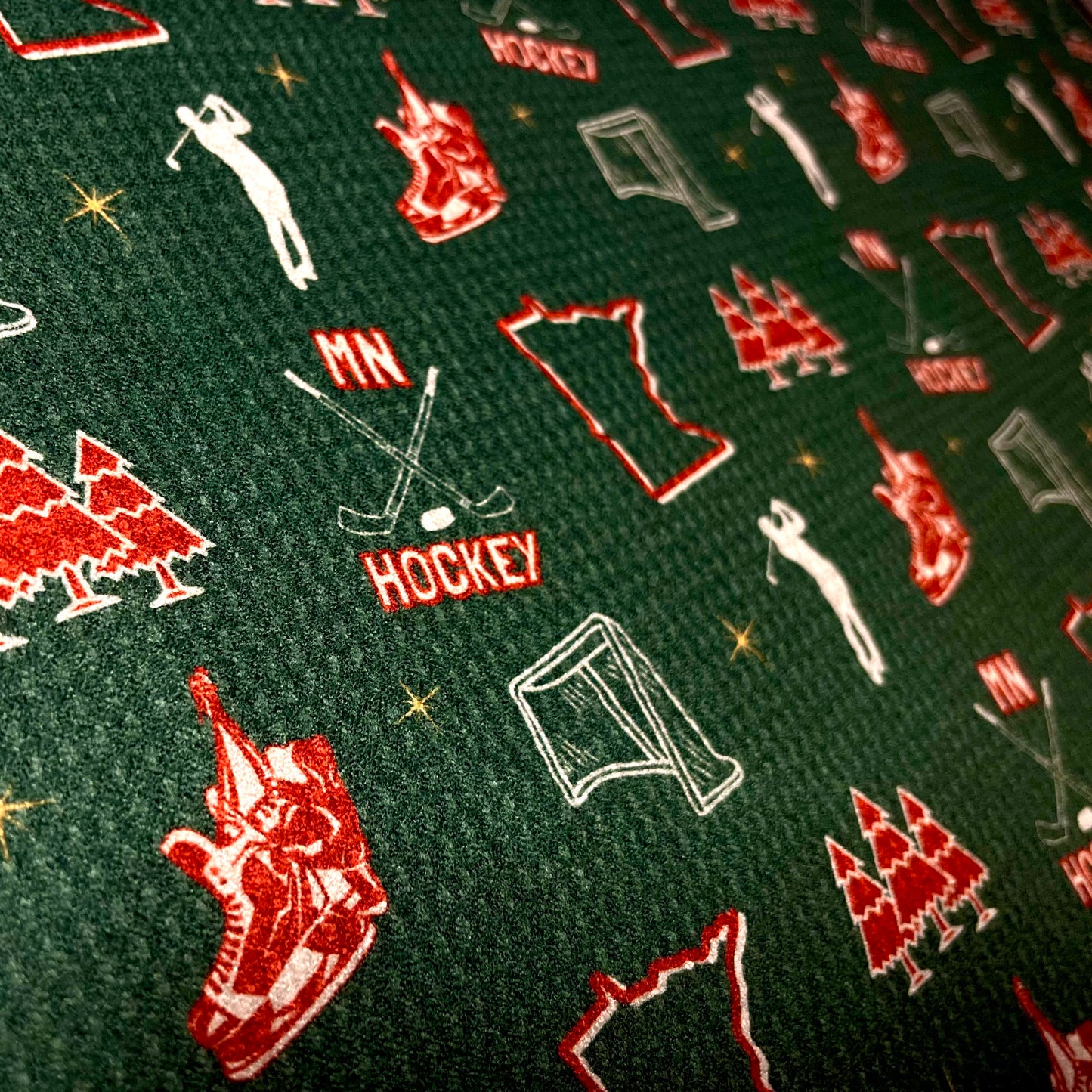 Close up of a green Minnesota Wild inspired hockey golf towel with red and white hockey, state, trees, skates, and golfer graphics.