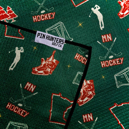 Close up of a green Minnesota Wild inspired hockey golf towel with Pin Hunters label, hockey sticks, skates, net, MN text, and Minnesota outline.