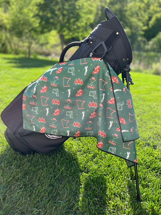 Green Minnesota Wild inspired hockey golf towel hanging from a black Pin Hunters golf bag with hockey skates, nets, MN text, Minnesota outlines, and golfer icons.