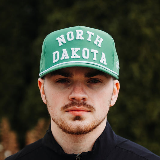 Green North Dakota performance golf hat with white raised embroidery, white rope detail, perforated side panels, and model front view.