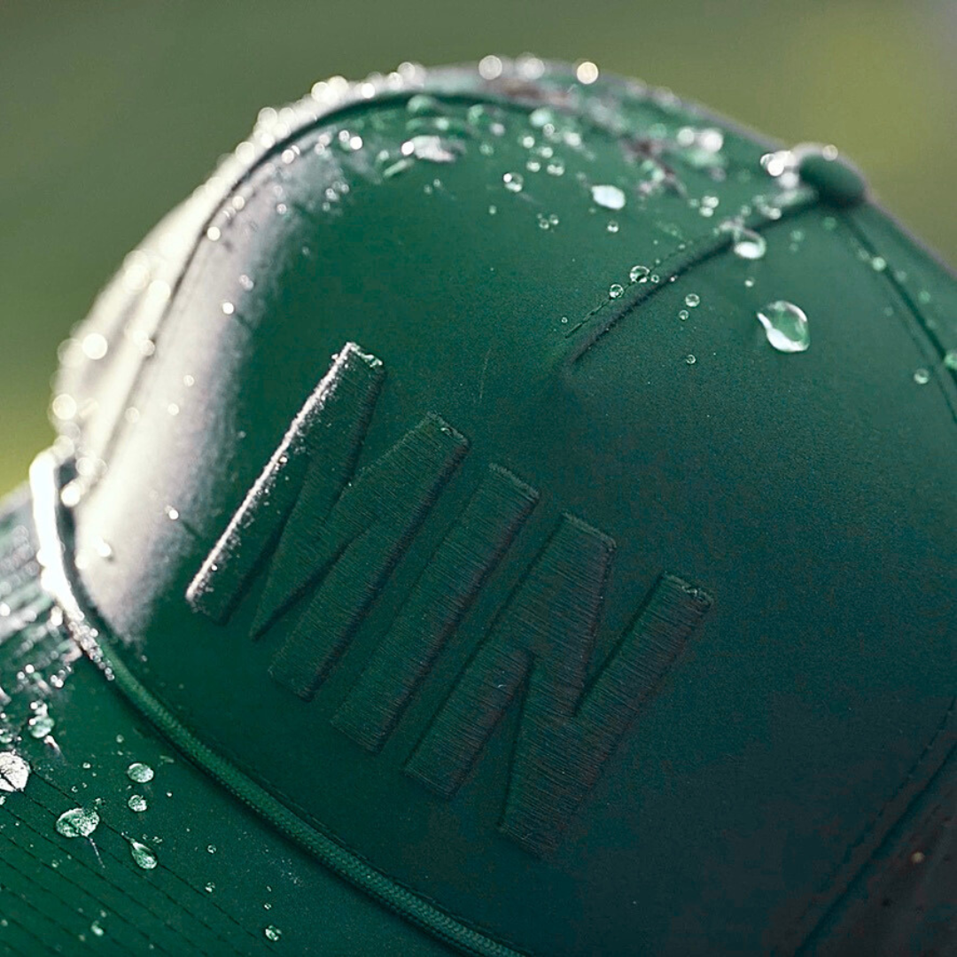 Green tonal MIN performance golf hat close-up with matching raised embroidery, water droplets, and green performance fabric.